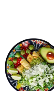 Enchiladas verdes topped with crumbled cheese, avocado, and lime on a colorful Talavera-style plate from Food Town